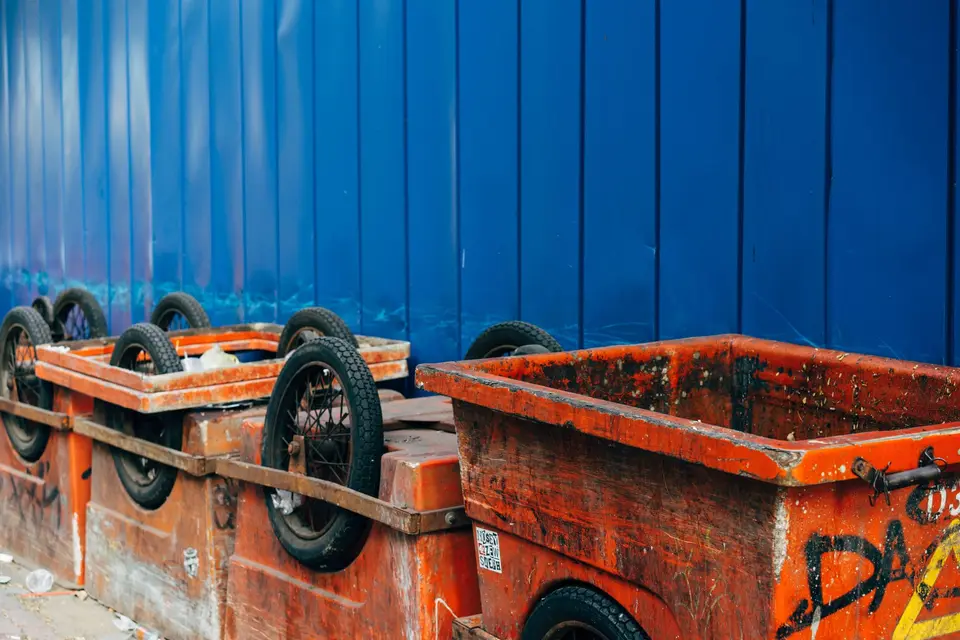 Bacs de chantier métalliques orange montés sur roues, devant une palissade bleue