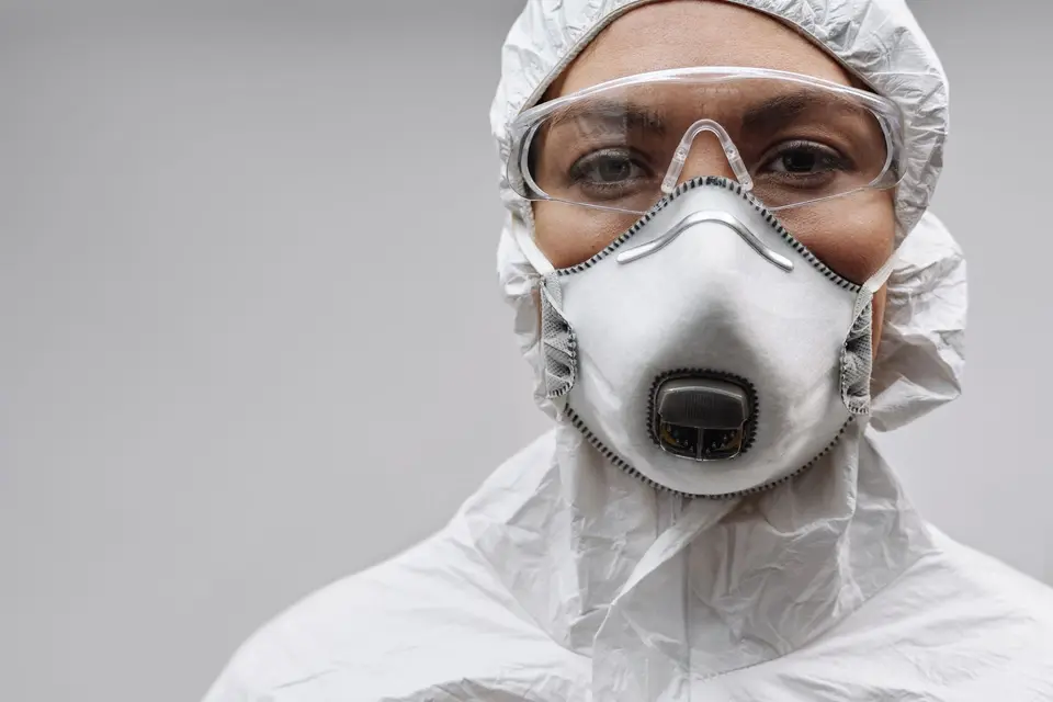 Personne en combinaison de protection blanche, avec lunettes et masque respiratoire