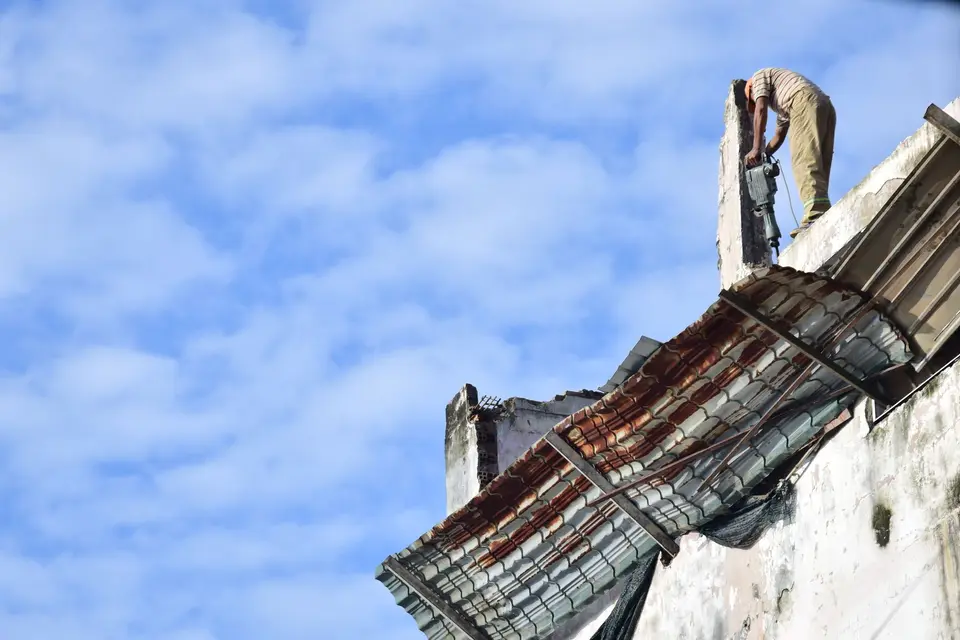 Ouvrier perché sur un mur, en train de démonter la toiture ondulée d'un vieux bâtiment